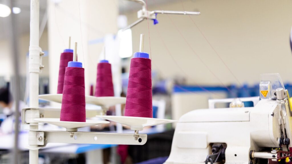 Garment manufacturing process in Bangladesh showing sewing machine and thread spools in apparel factory